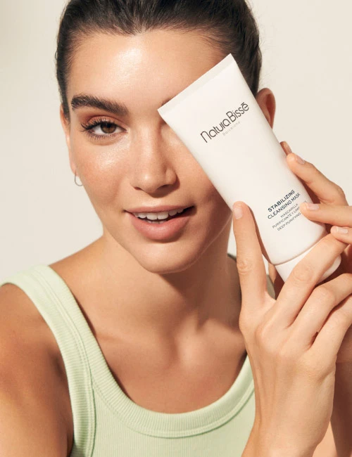 Woman holding Natura Bissé's Stabilizing Cleansing Mask. Skincare product featured in bestsellers.