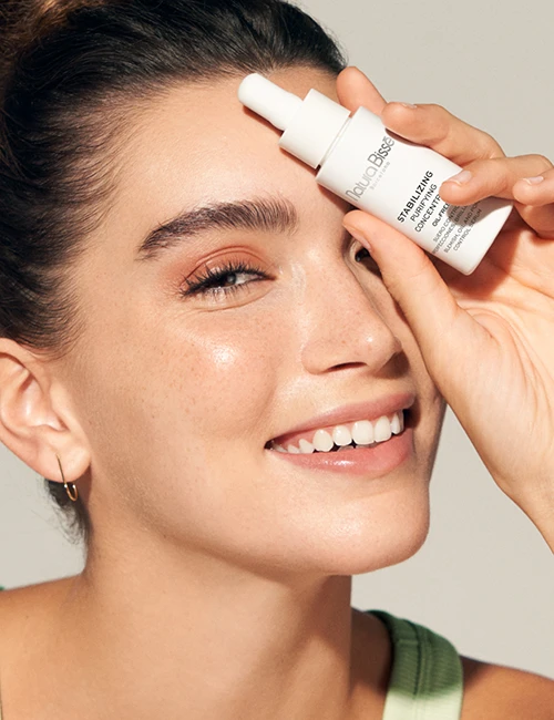 Mujer sonriendo y sosteniendo Stabilizing Purifying Concentrate frente a su cara. Producto presentado en nuestros bestsellers.